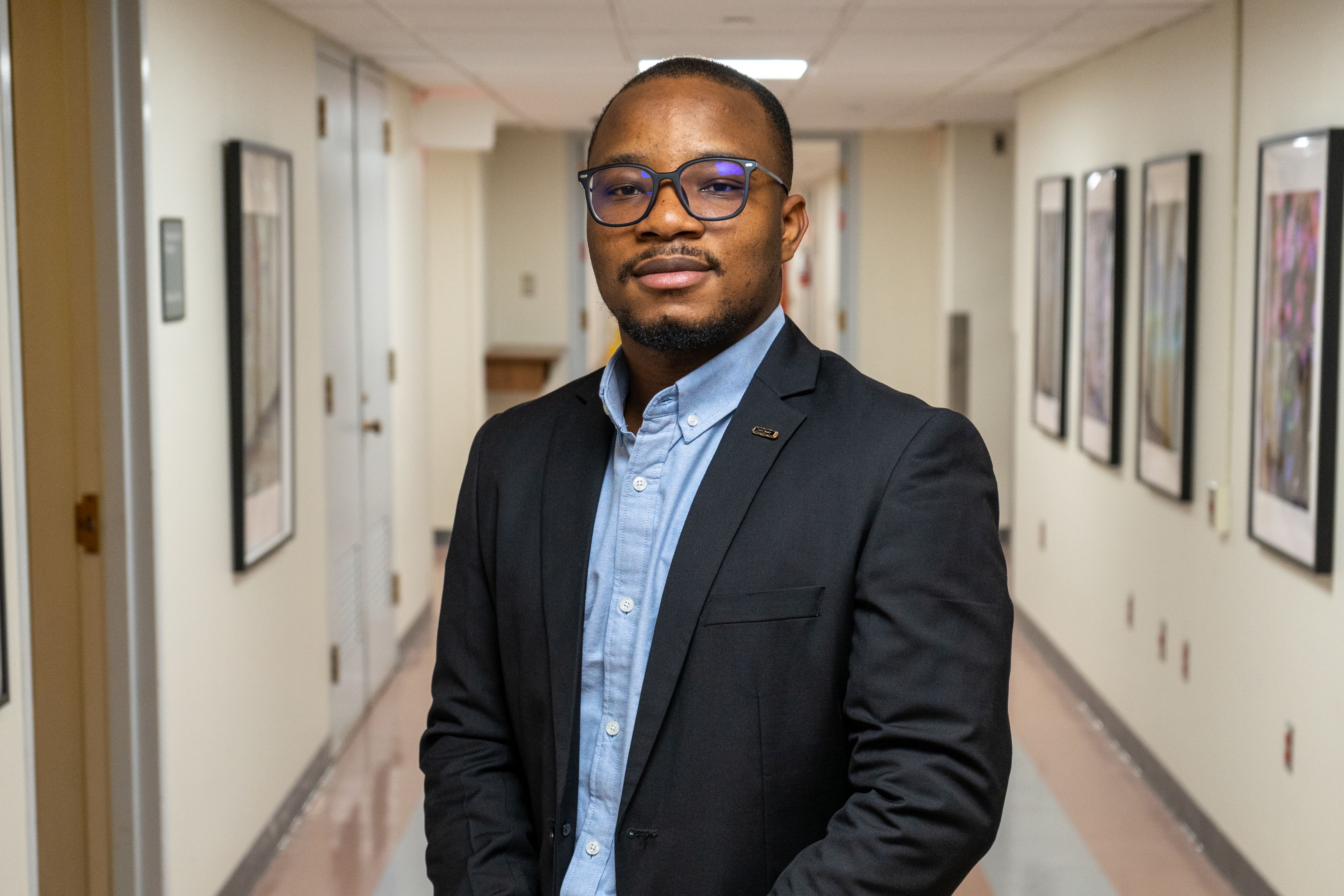 Tunde Oyebamiji wearing a suit and glasses in a corridor