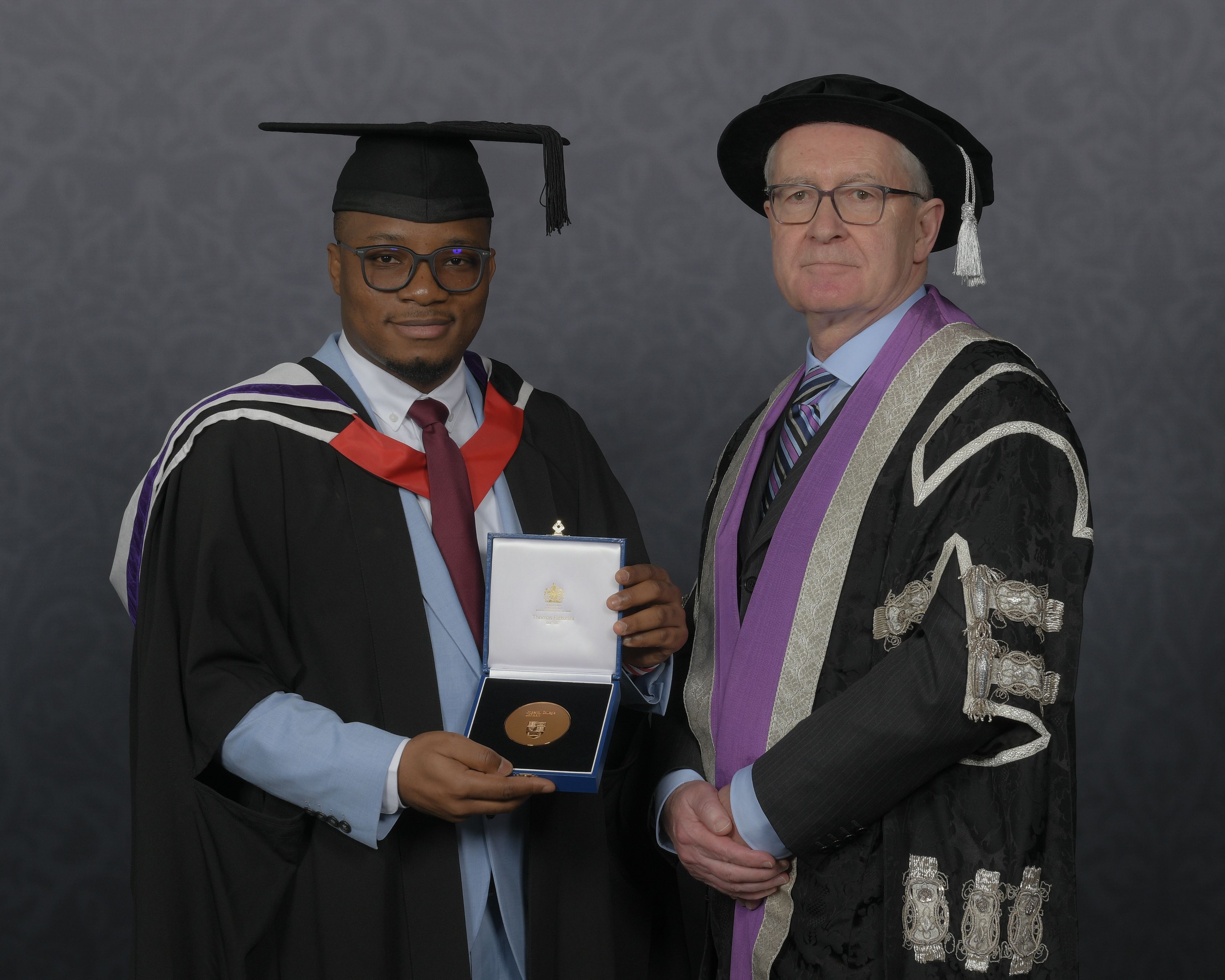 Tunde in a graduation gown and hat receiving the Student Award for Outstanding Achievement at his graduation from Imperial President Hugh Brady