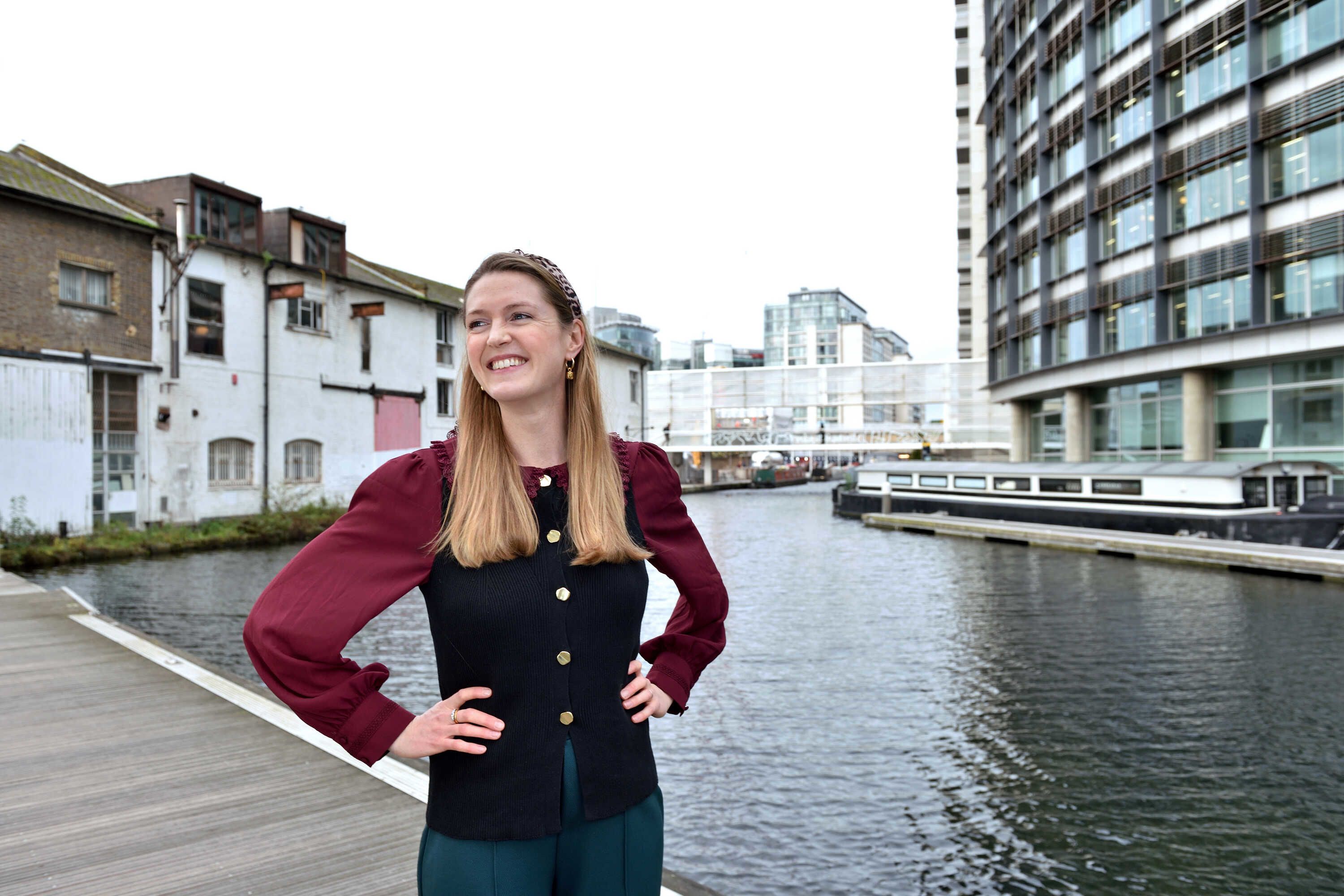 Anna with her hands on her hips smiling while looking to the left of the camera, standing in front of the developing Fleming Centre near the canals behind St Mary's Hospital.