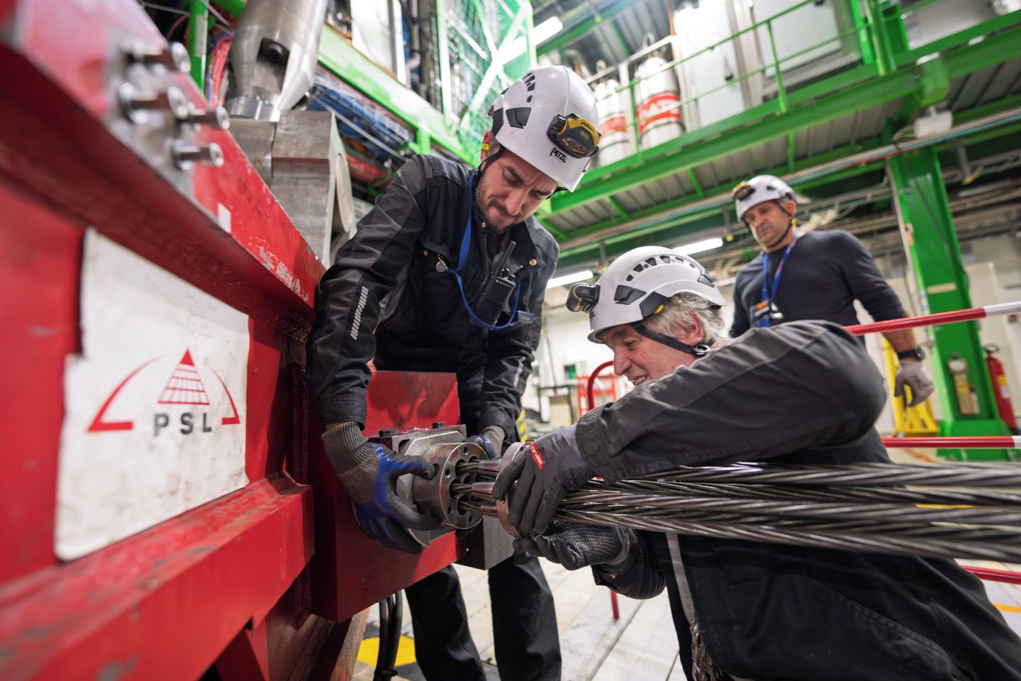 People in hardhats and protective war, assembling the CMS' components. One person is holding a component in place, while the other runs wires through its barrels.