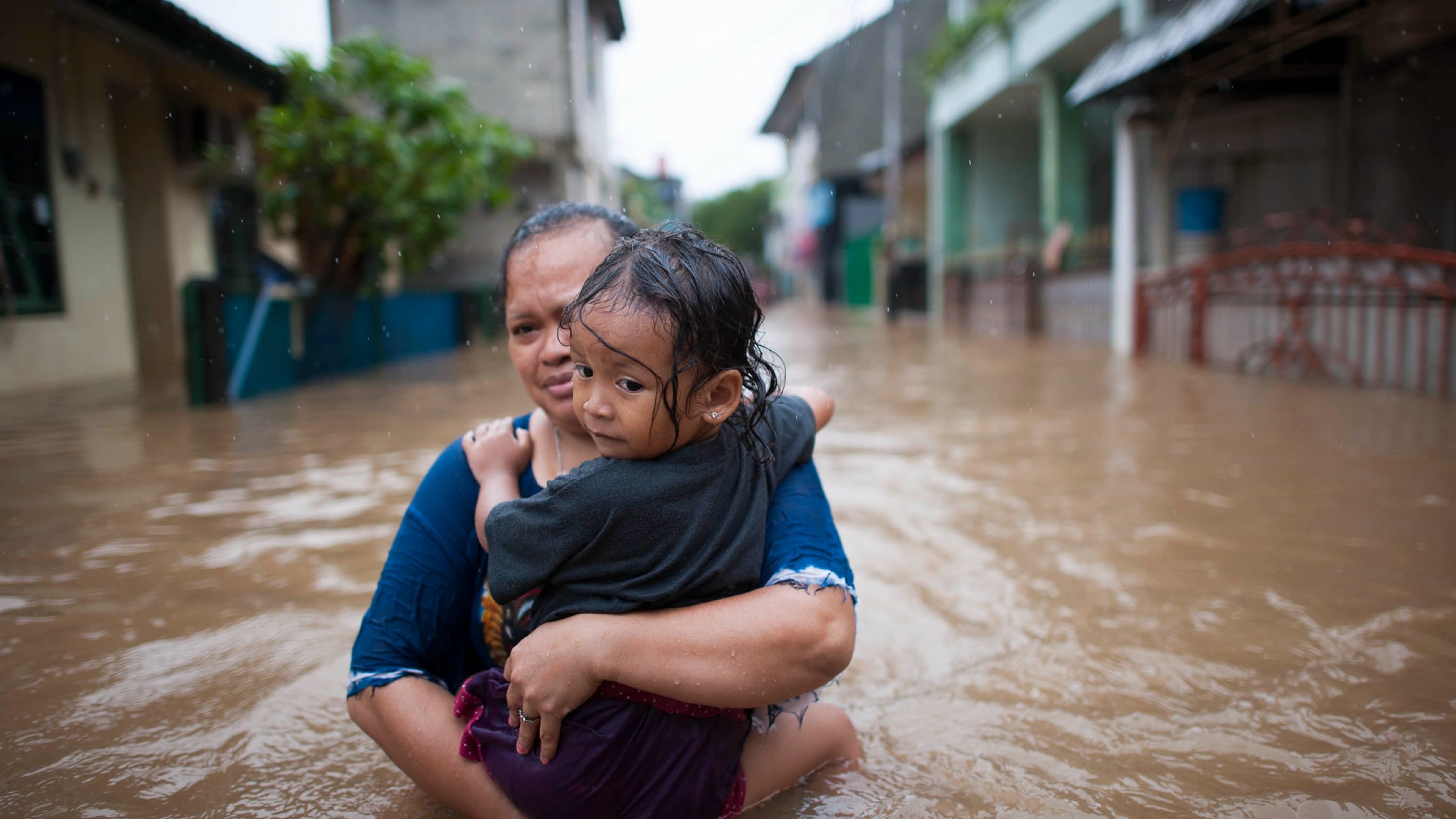 An adult and a child walking through flood water.