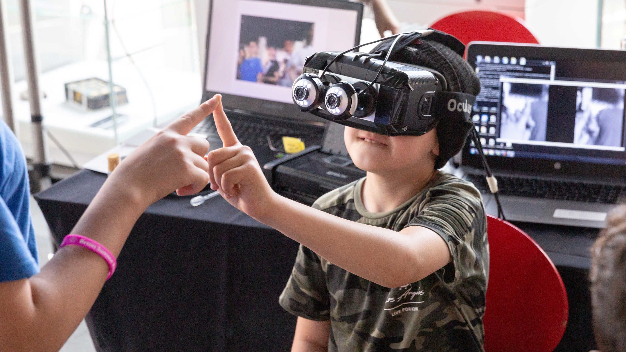 A young boy with VR goggles touching index fingers with a scientist