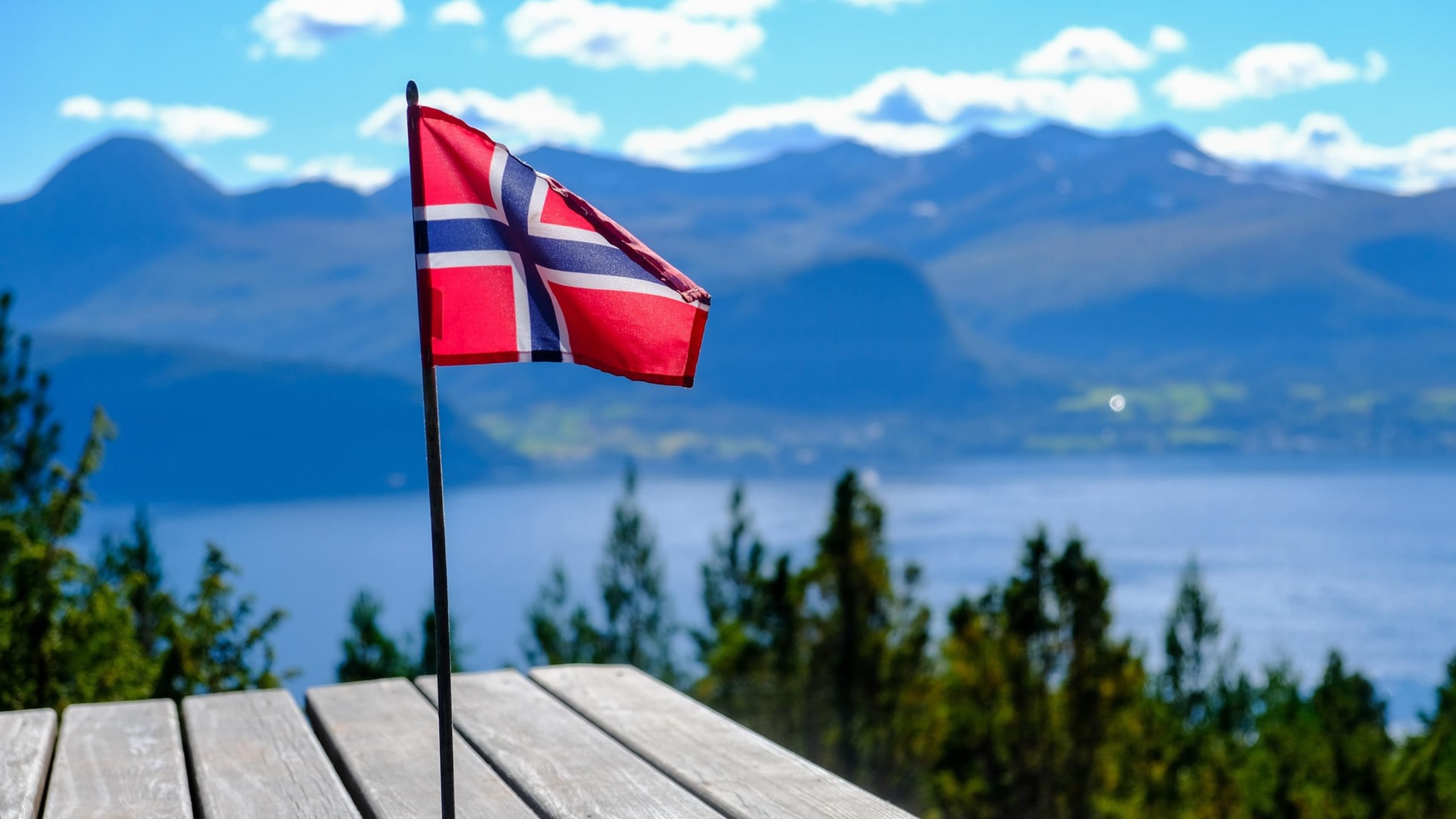 The Norwegian flag with a lake and mountains in the background