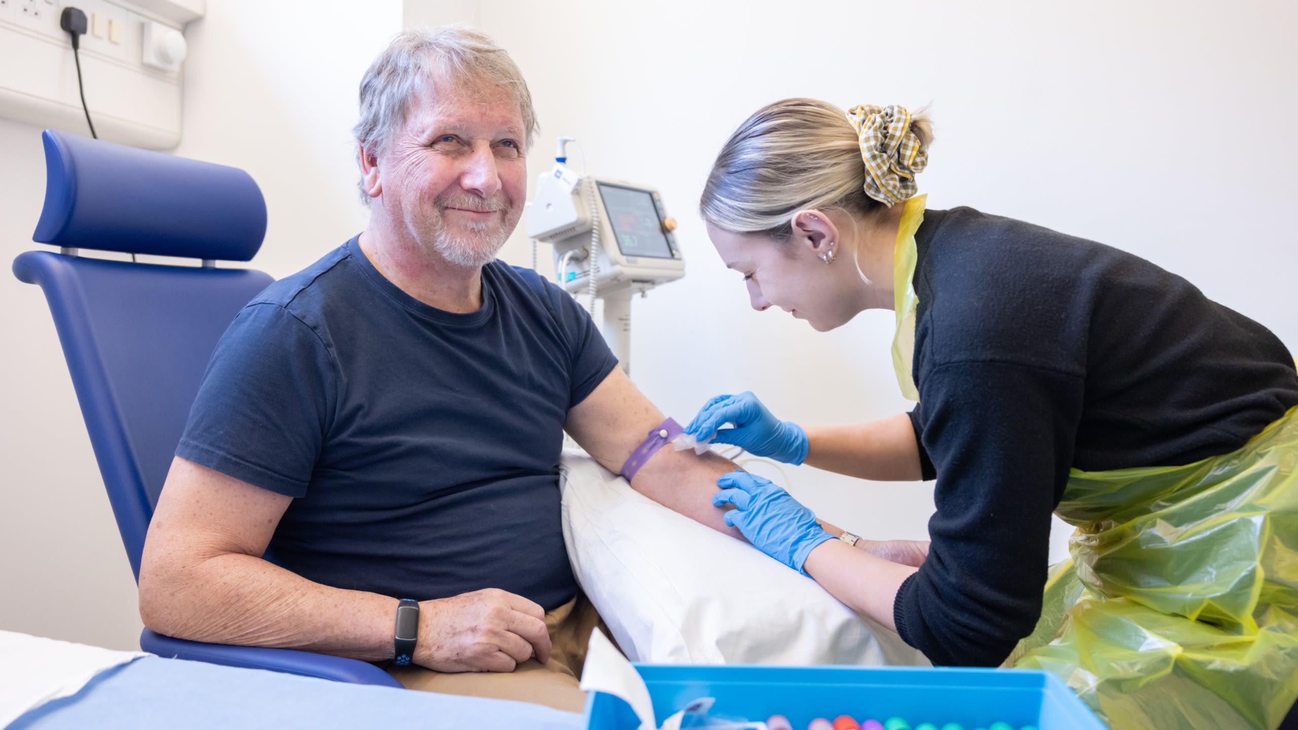 A nurse sanitises a smiling, male patient's left arm in preparation for drawing blood