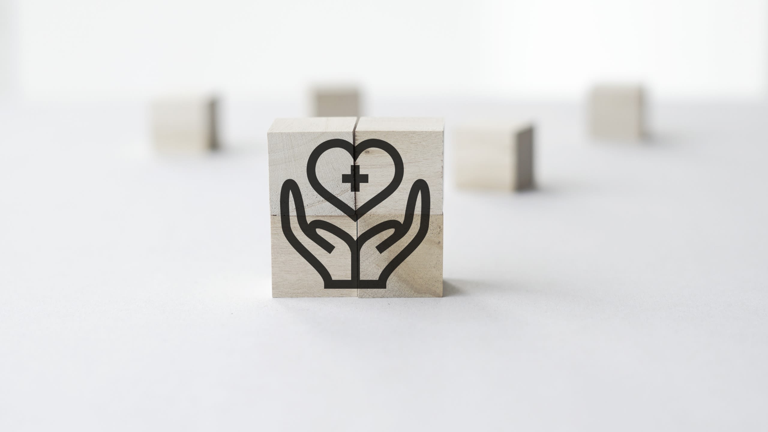 Two wooden blocks printed with an image of hands holding a heart with a medical cross on it