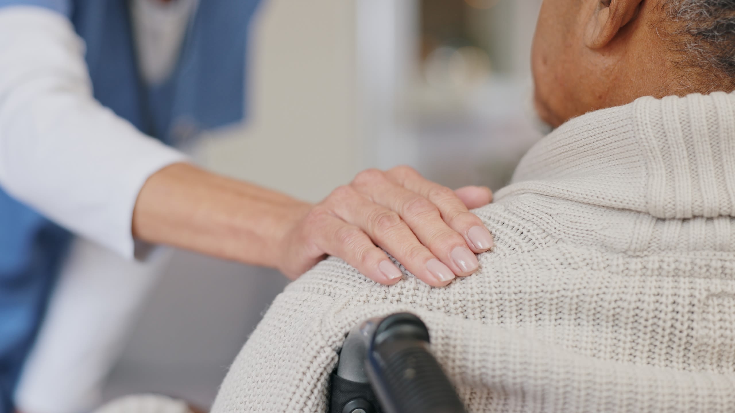 A nurse with her right hand on a male patient's shoulder, showing empathy