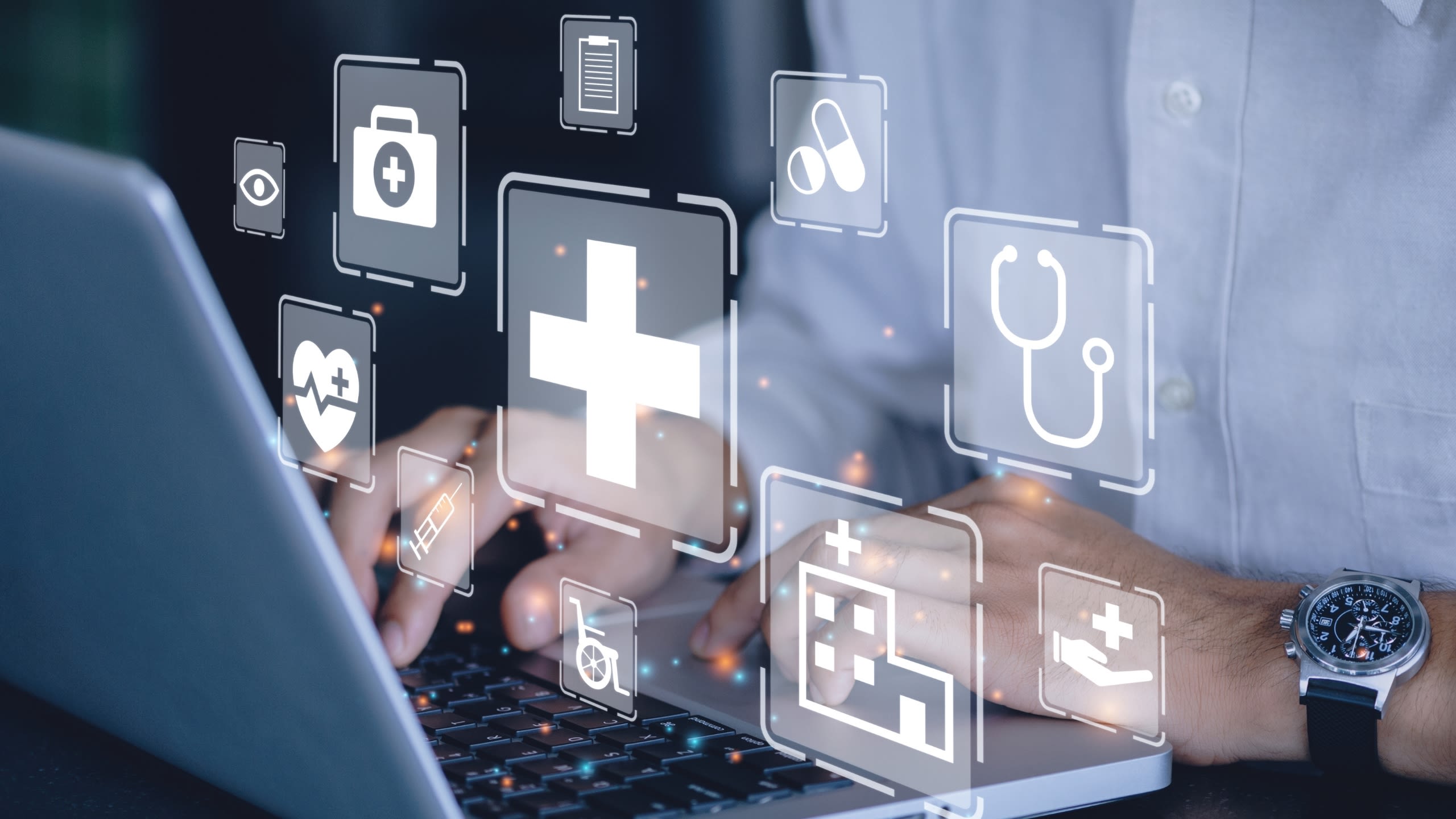 A man types on a laptop keyboard. The image is overlaid with transparent medical symbols including a heart, a stethoscope and a hospital.