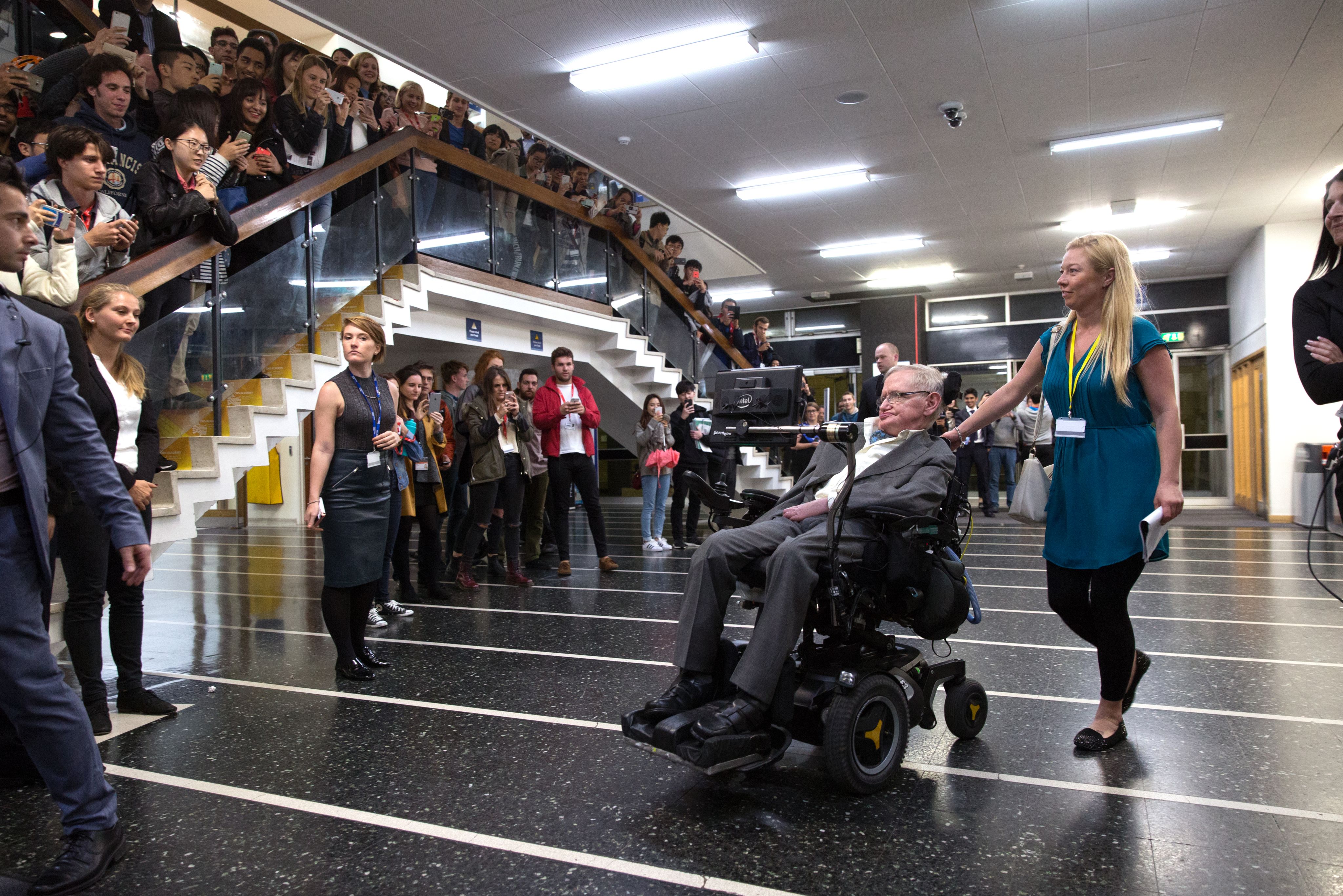 A photograph of Professor Stephen Hawking outside the Great Hall. The stairs are full of students who have come to attend Hawking's lecture.