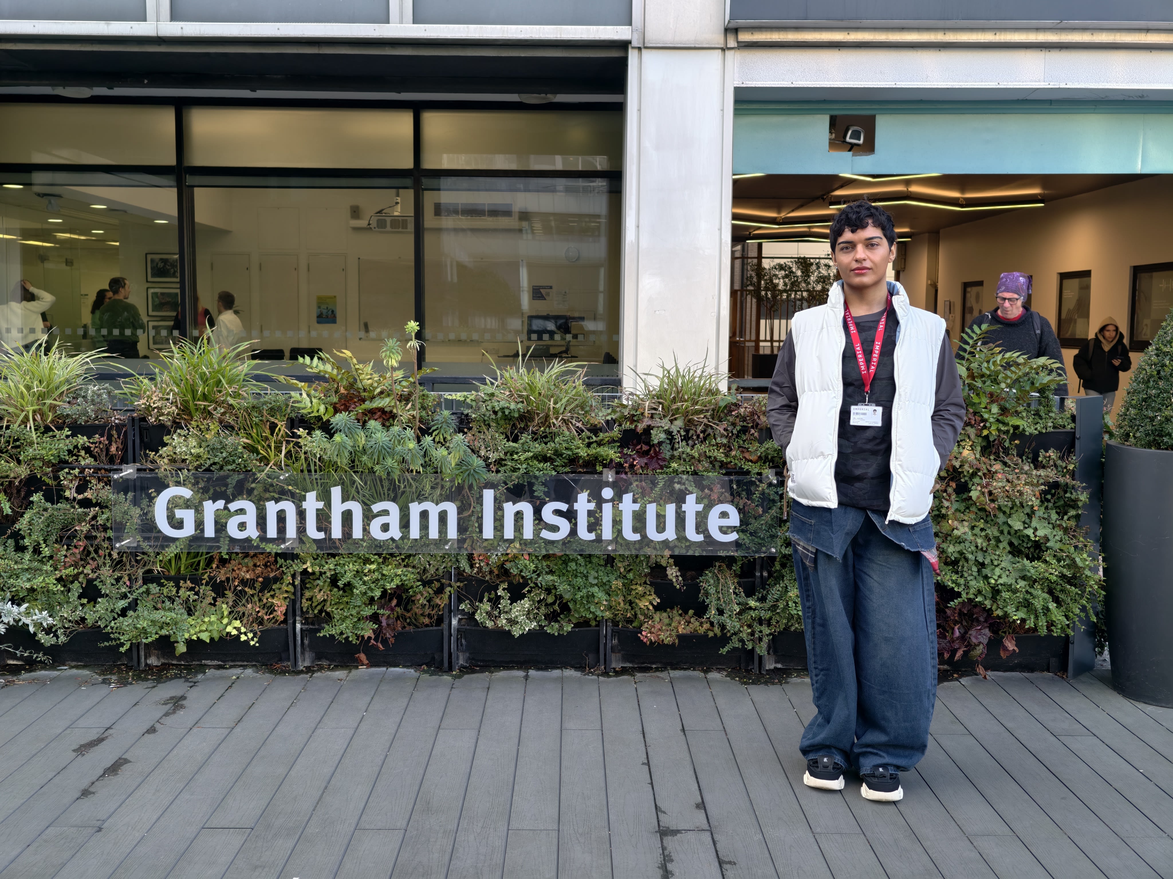 Emil standing by a plant wall with a 'Grantham Institute' sign