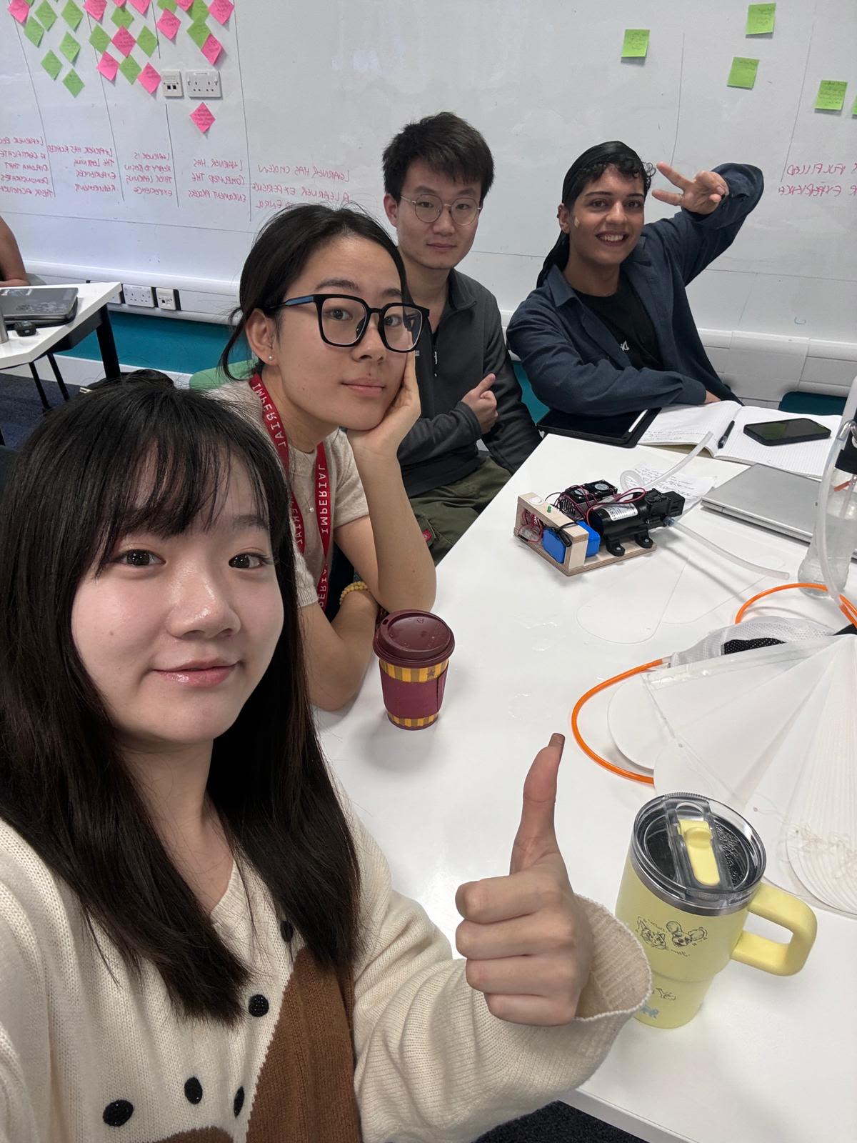 Emil with his coursemates sat around a table with a big whiteboard with post-its on in the background