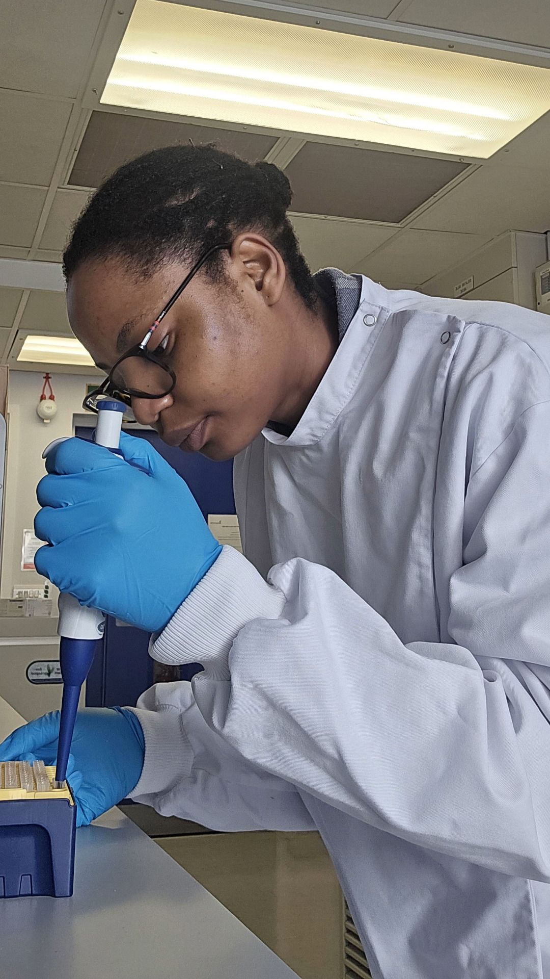 Folakemi wearing a lab coat and gloves while using a pipette in the lab