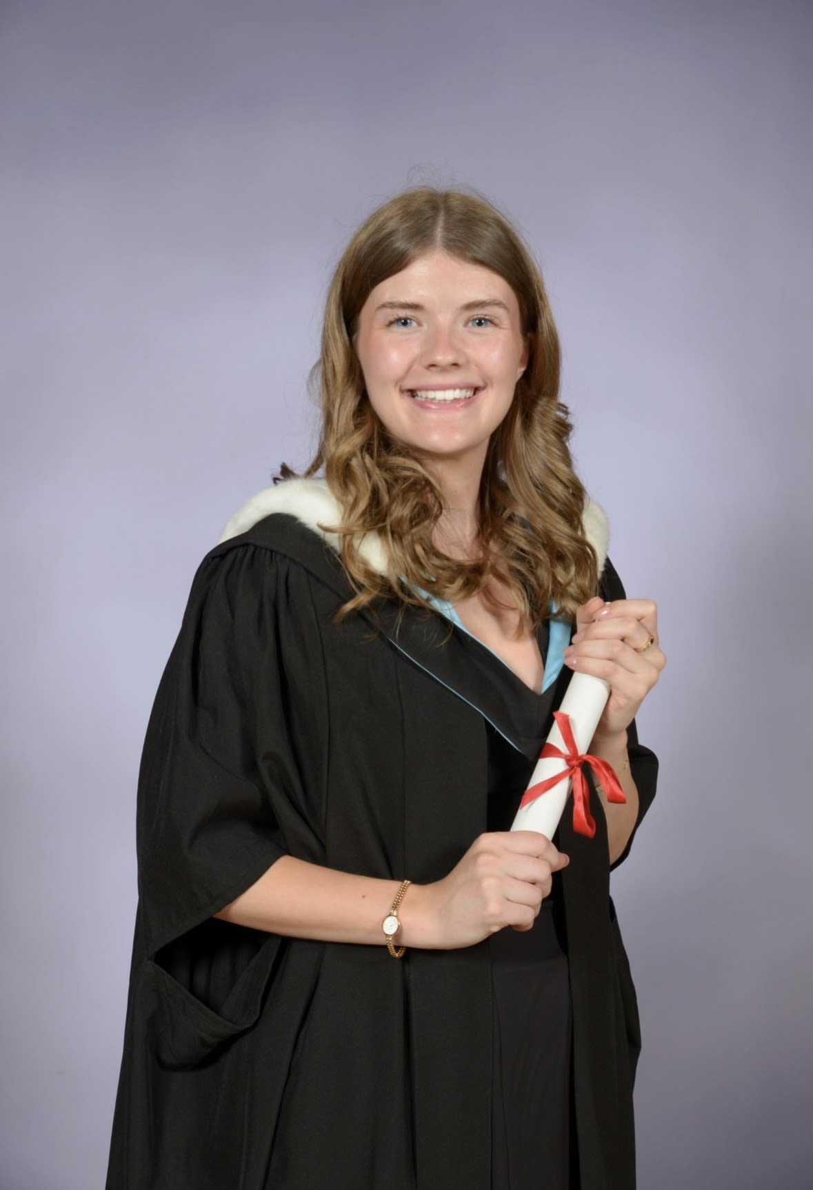 Hannah wearing a graduation gown and holding a rolled up certificate with a red bow