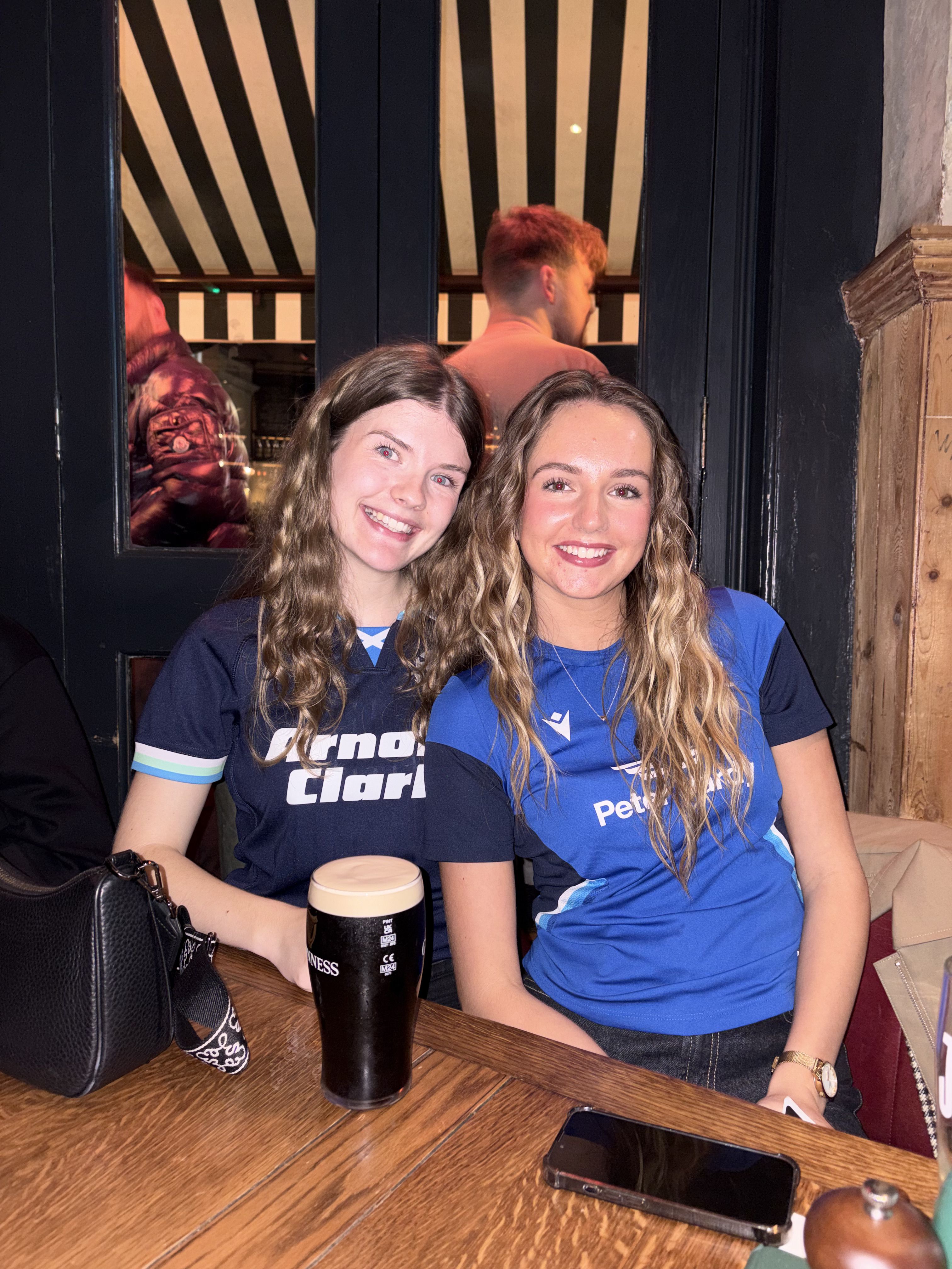 Hannah in a pub with a friend. A pint of Guinness is on the table in front of them
