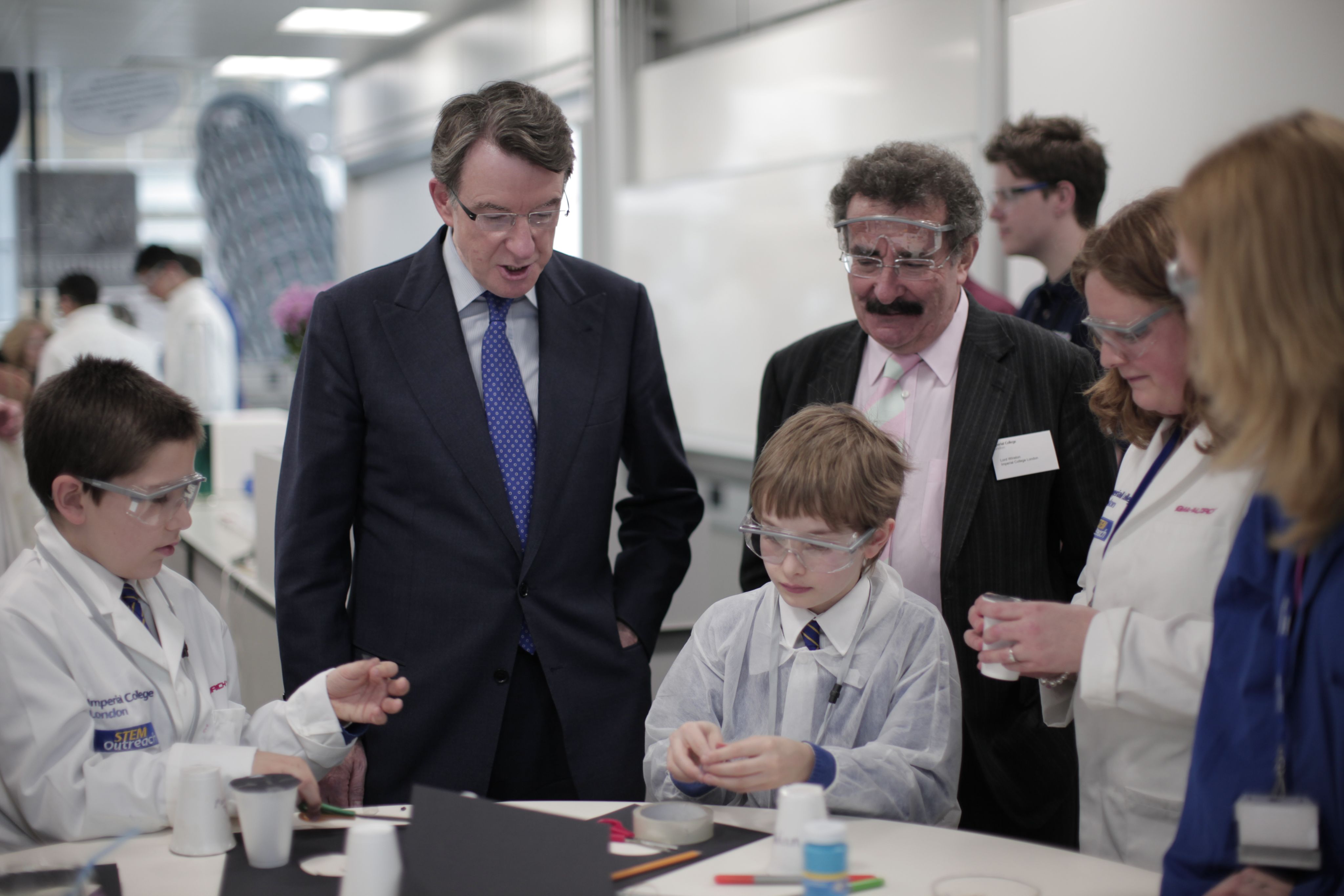Peter Mandelson and Robert Winston in the Reach Out lab with children in lab coats sat at a lab bench doing science activities