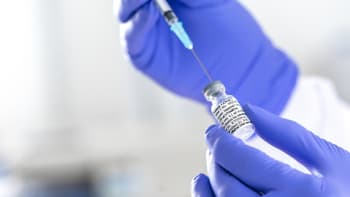 A vial of COVID-19 vaccine with a syringe taking liquid from it.