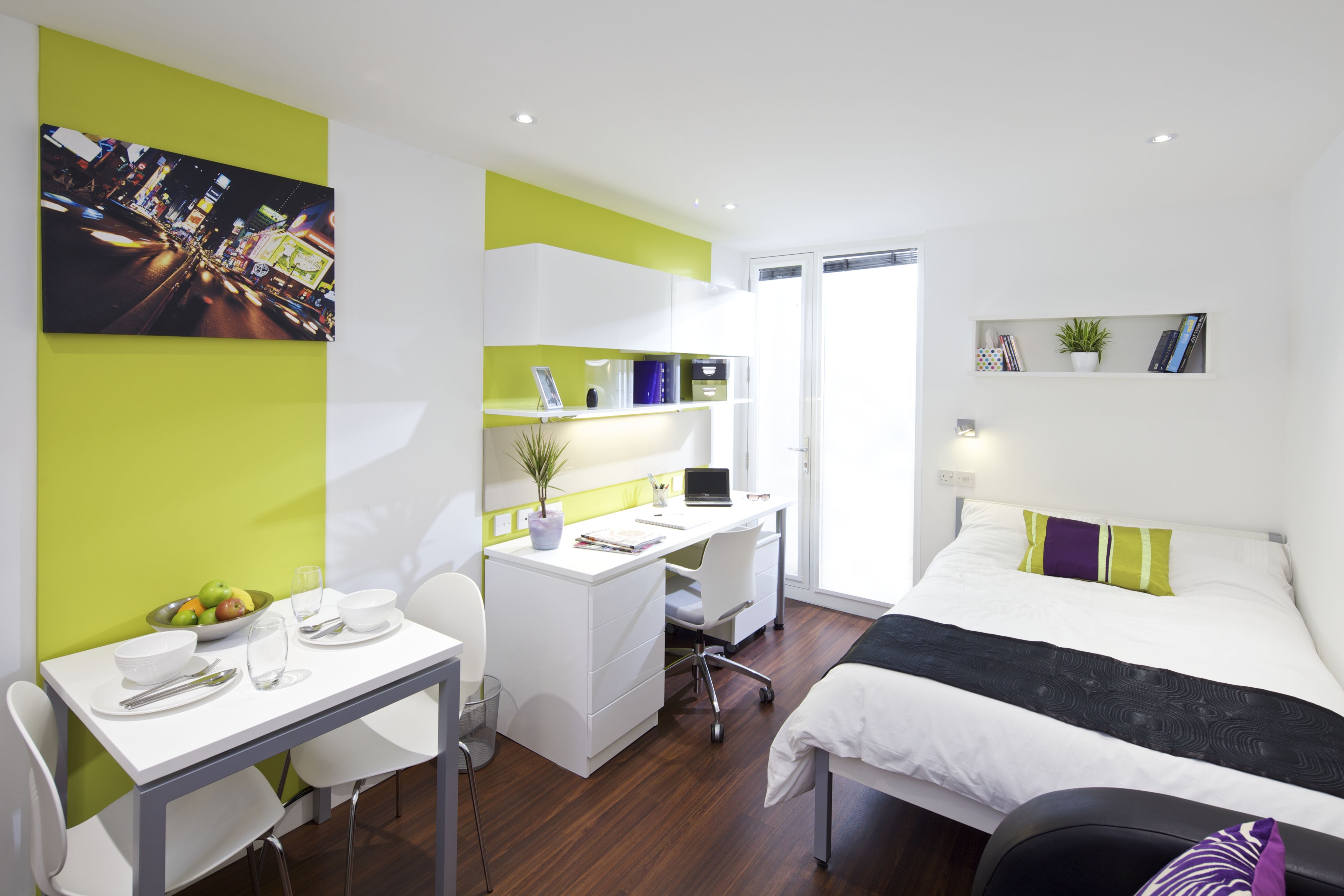 A studio room with a desk and chair, shelves, a dining table and a bed