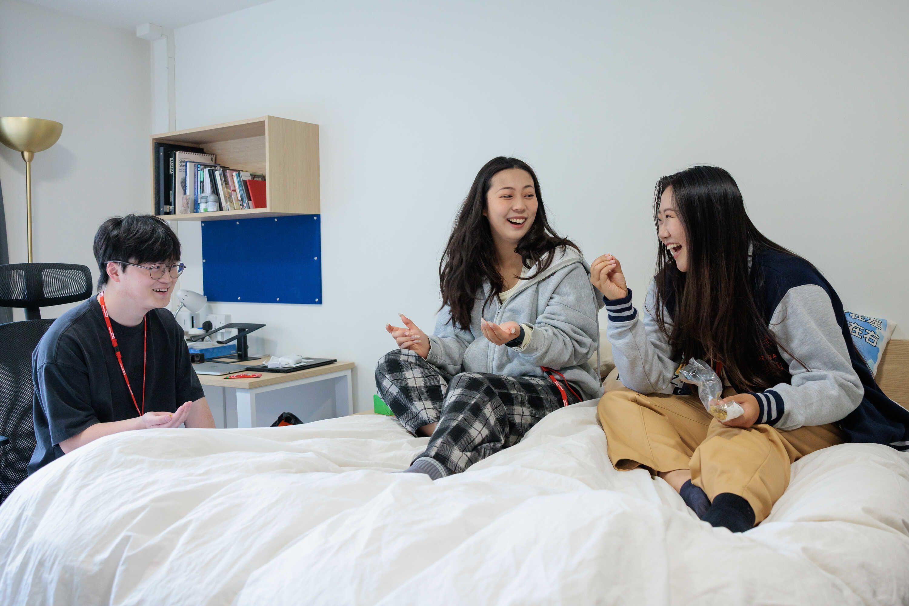 Two students laughing while wearing loungewear and sitting on bed