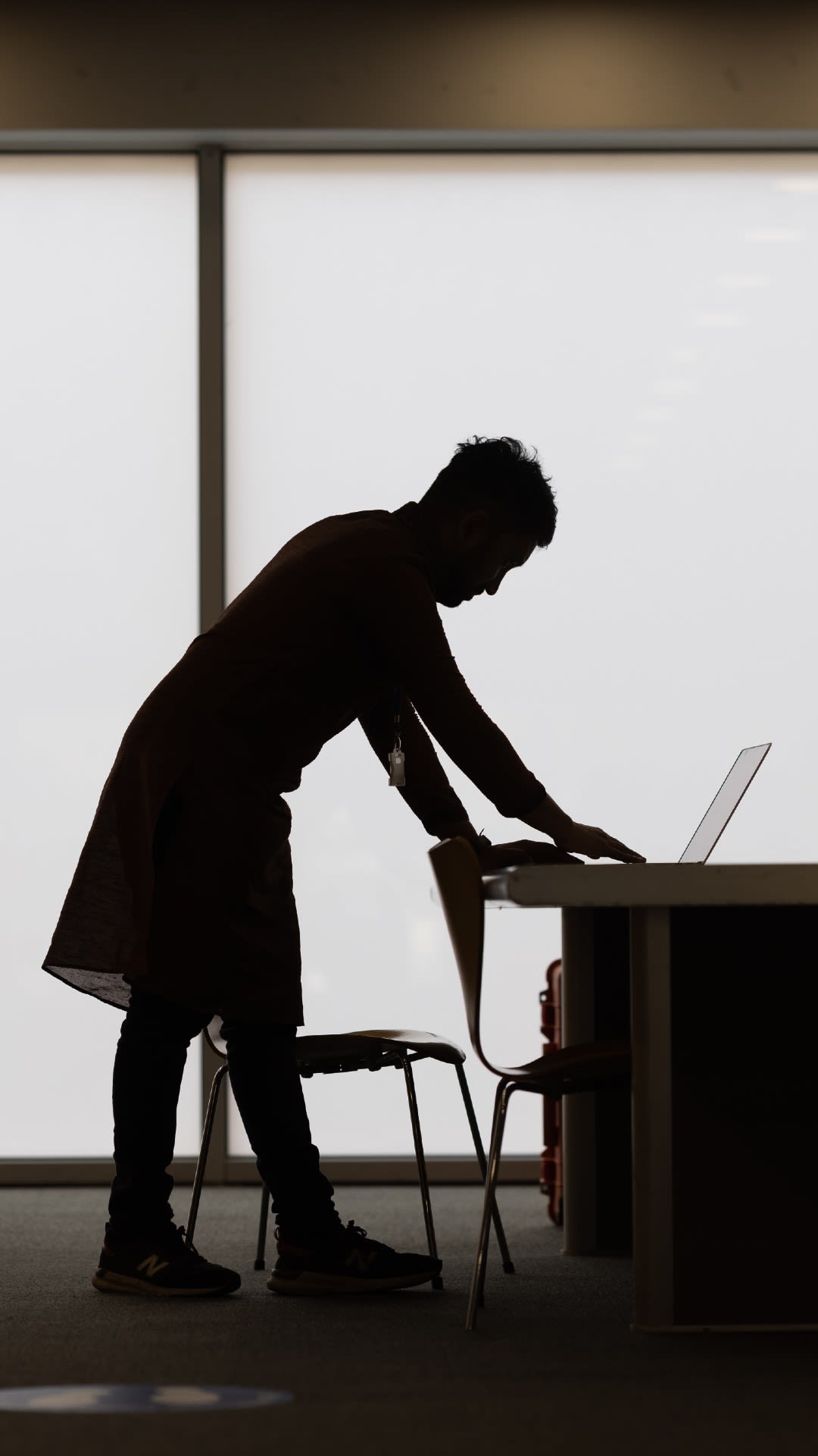 A silhouette of Sohag leaning over a laptop