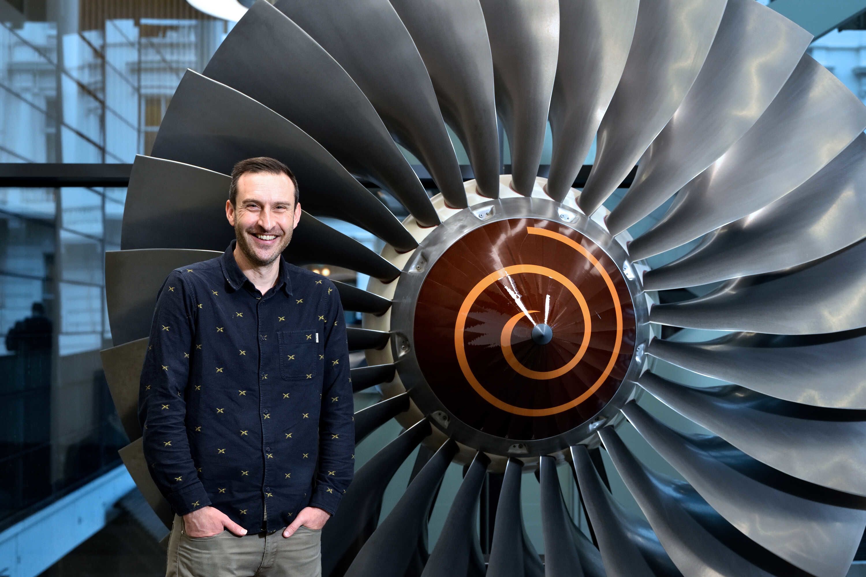 Simon Foster standing in front of a large grey propellor smiling at the camera