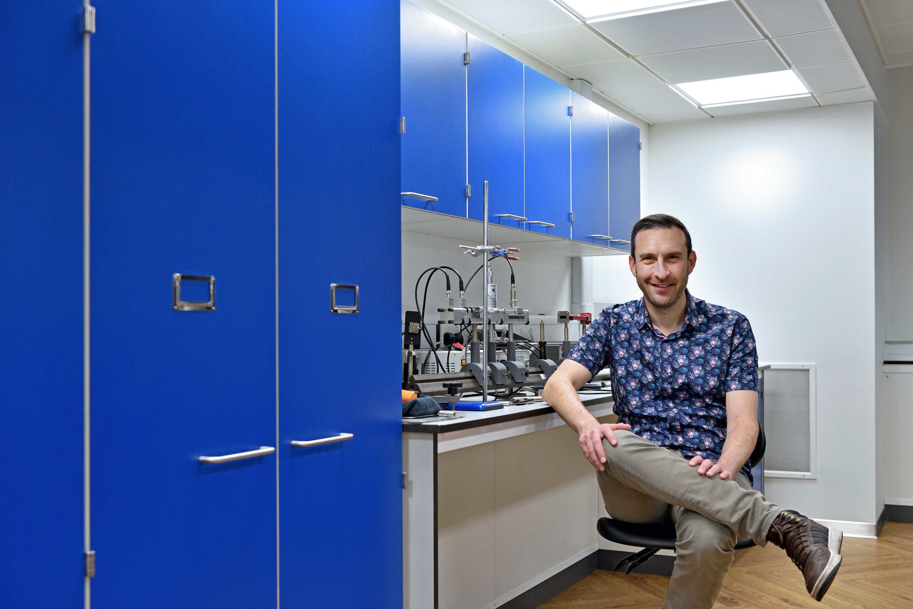 Simon captured sitting on a chair in front of a technology lab bench with his legs crossed.