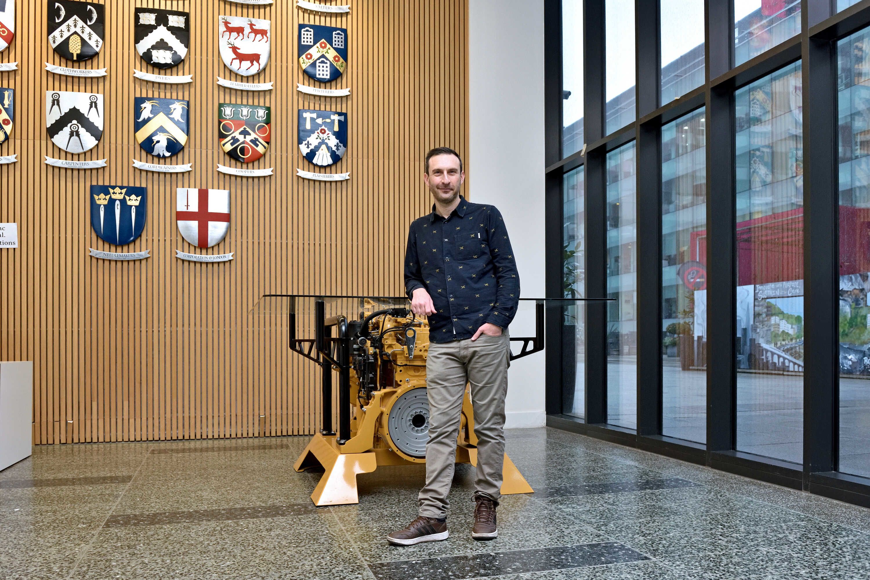 Simon captured leaning with one arm on a glass table which base is made up of machinery.