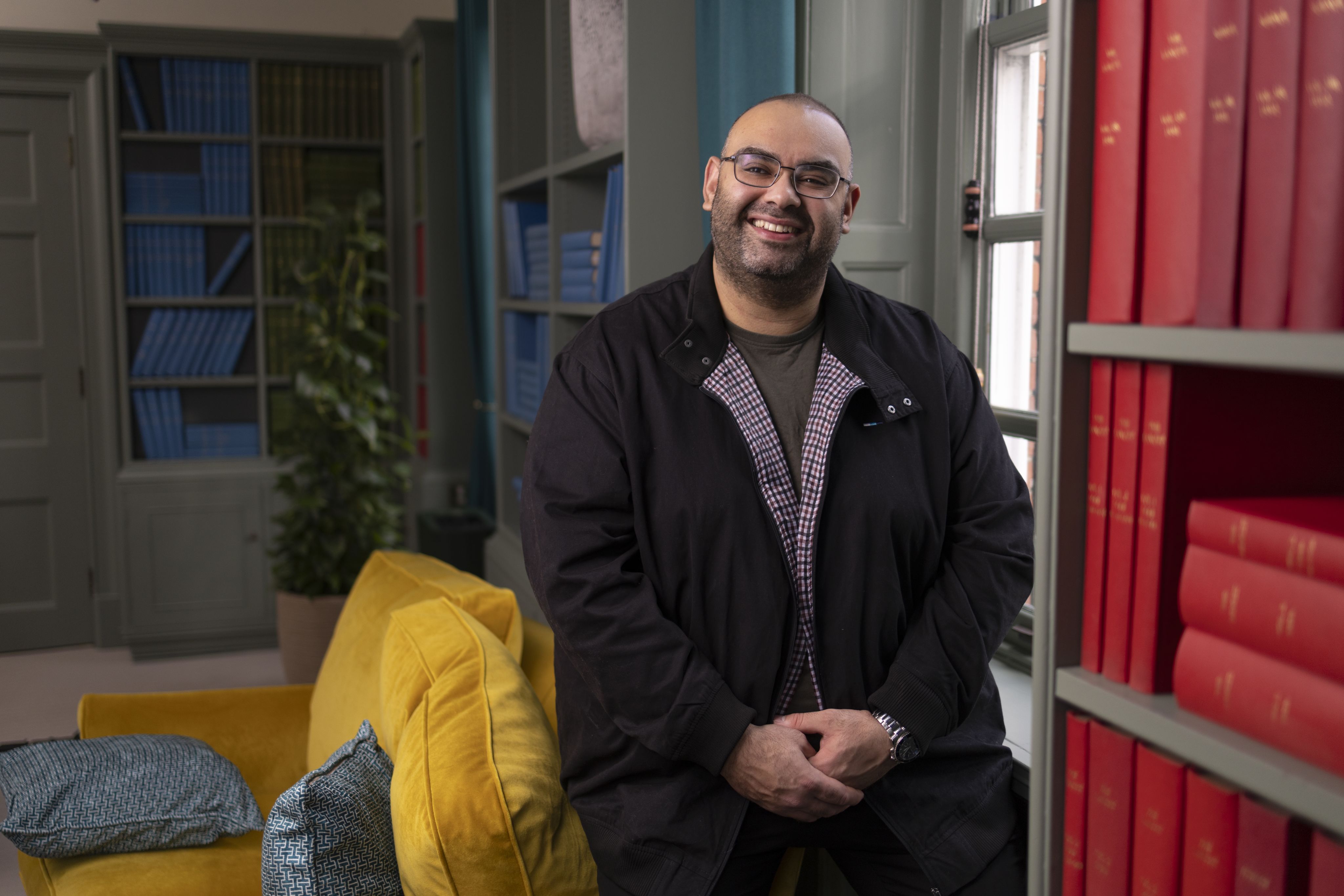 Kyrillos smiling in a colourful room with tall bookcases