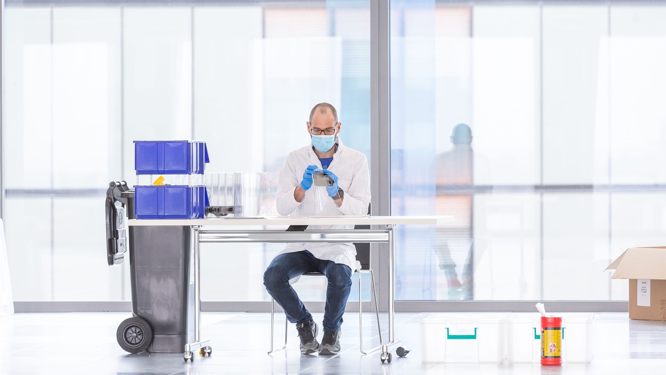 David Miller sits at a table making a disposable visor for medical workers