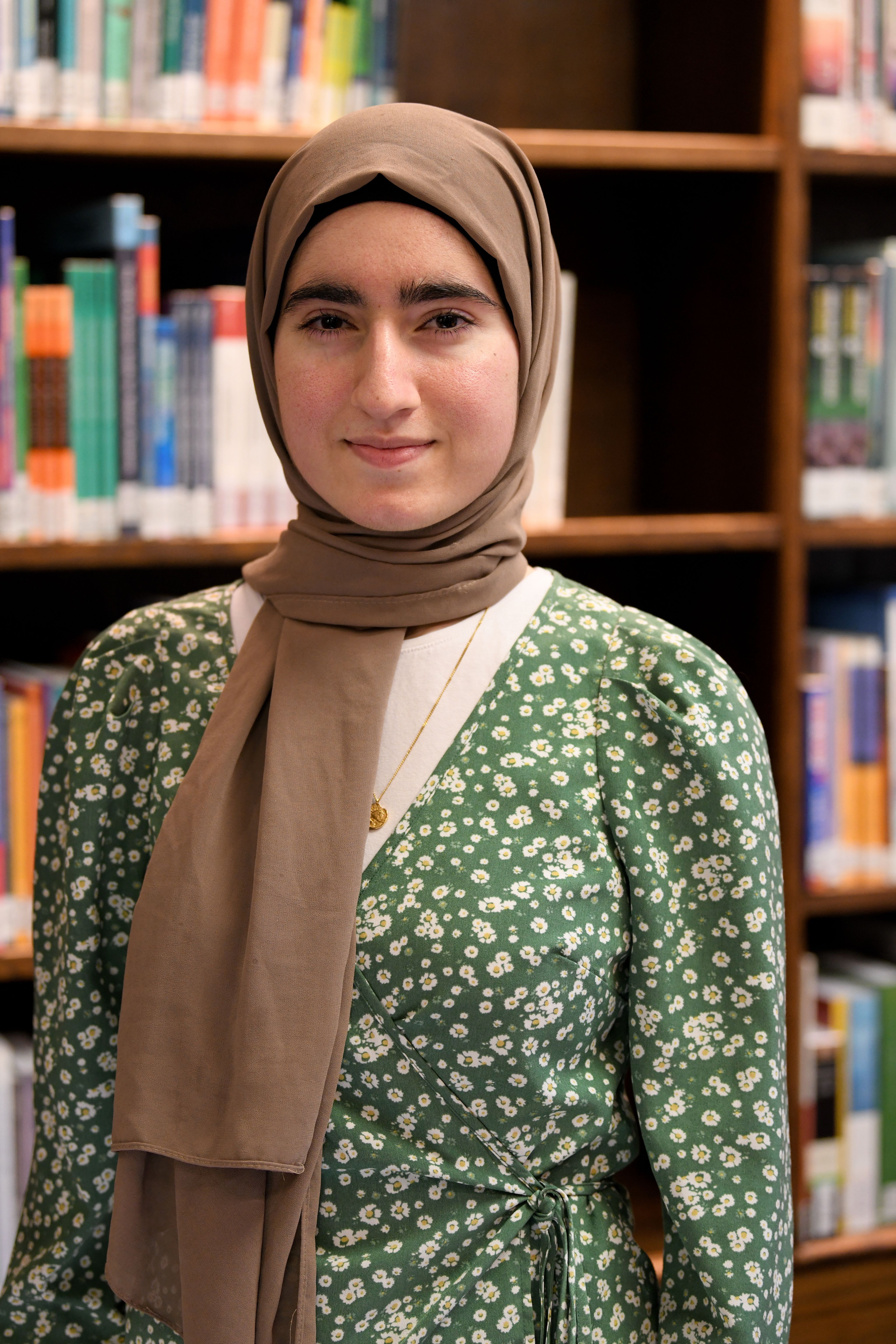 Isra is a second year medical student and is standing in front of some bookshelves in a library