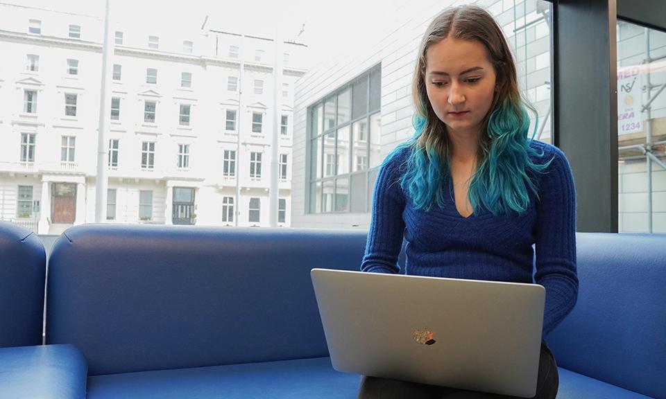 Woman sitting on blue sofa on laptop