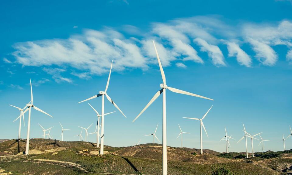 Wind turbines on a green hilltop with bright blue sky in the background