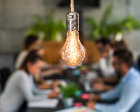 Lightbulb in foreground with table of people behind 