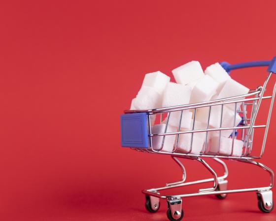 A shopping trolley is filled with refined sugar cubes on a red background