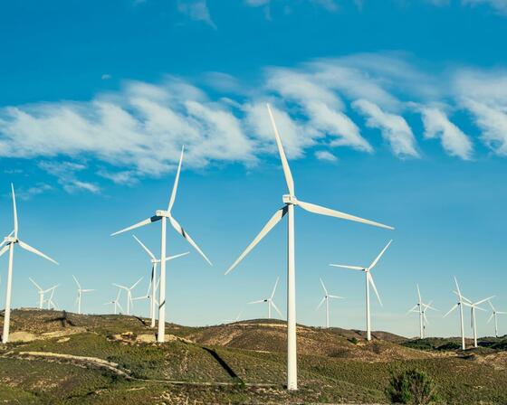 Wind turbines on a green hilltop with bright blue sky in the background