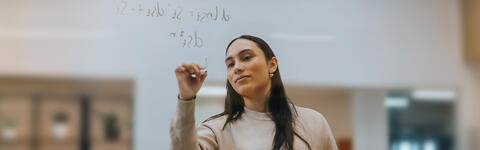 Imperial MSc Finance student on campus in London writing an equation on a clear board 