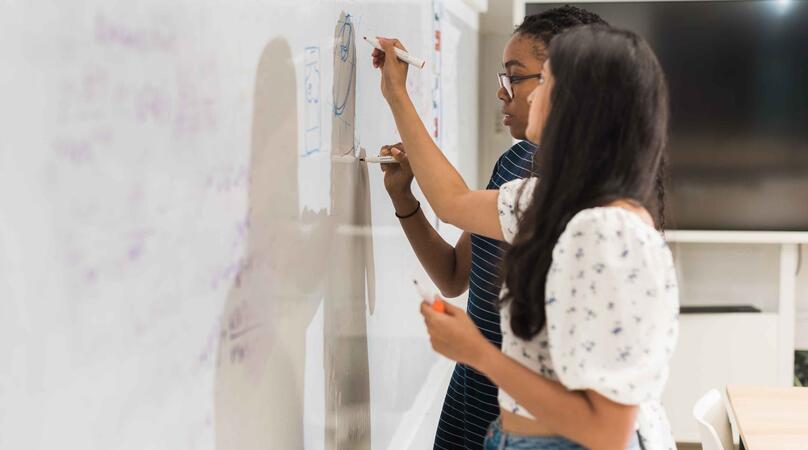 Two MSc Risk Management & Financial Engineering students writing formulas on a whiteboard