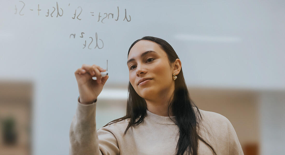 Imperial MSc Finance student on campus in London writing an equation on a clear board 