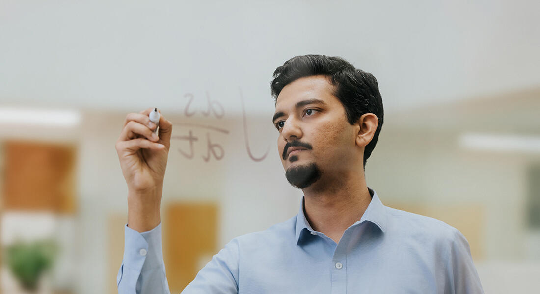 Imperial MSc Financial Technology student on campus in London writing an equation on a clear board 
