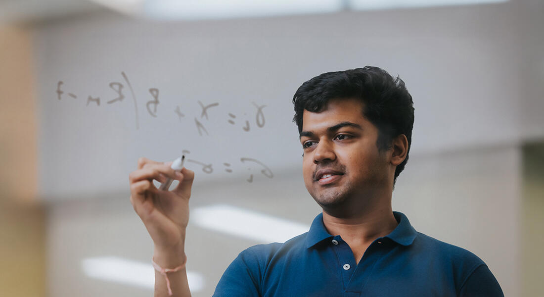 Imperial MSc Investment & Wealth Management student on campus in London writing an equation on a clear board 