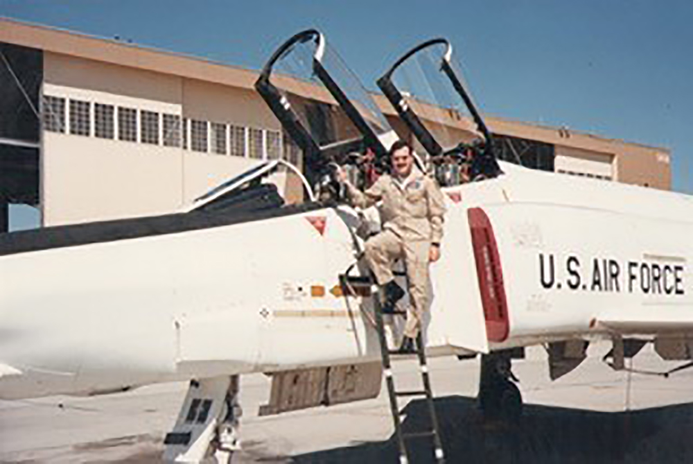 Old photograph of a young John Maris standing on a ladder leaning next to a US Air Force small plane