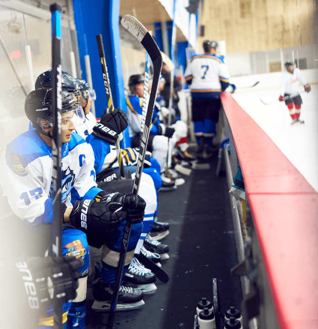 Ice hockey players sitting at the side of a skating rink during a match