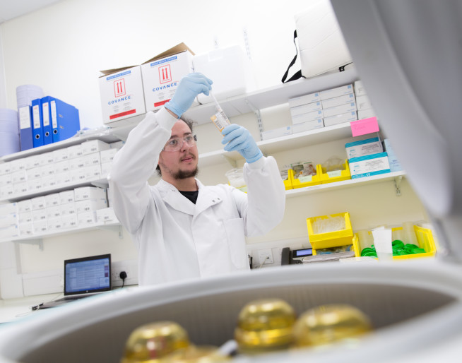 A researcher prepares a sample for testing. He is bearded and wears a white lab coat.