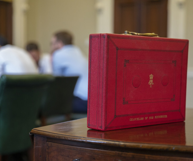 Chancellor of the Exchequer red box on a wooden table with people at a meeting table in the background.