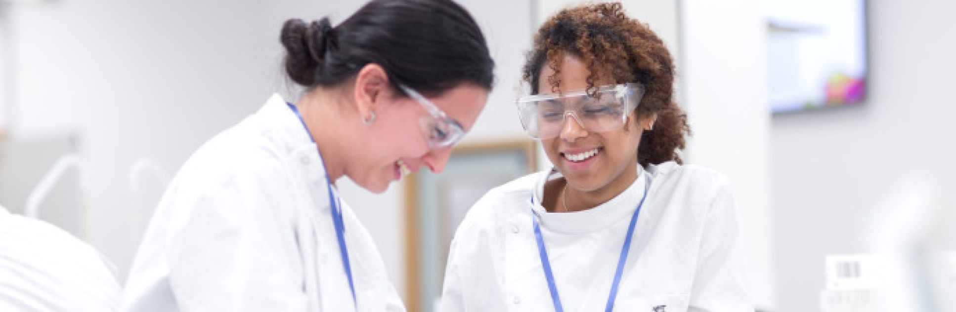 Two women in lab smiling whilst carrying out an experiment