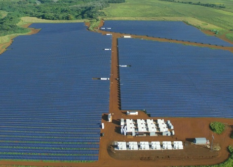 A large field of solar panels with large, white batteries at one end
