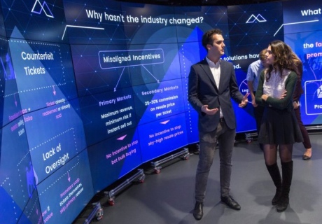 A man and woman discussing something next to a large screen showing words and diagrams.
