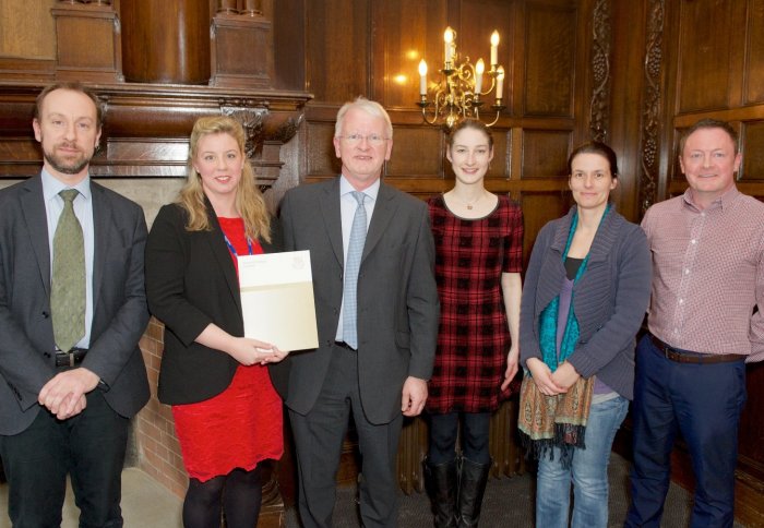 people standing in line with certificate with wood-pannelling in background