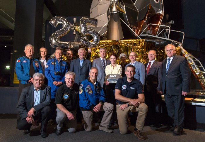 15 astronauts with cake and balloons in front of mood lander