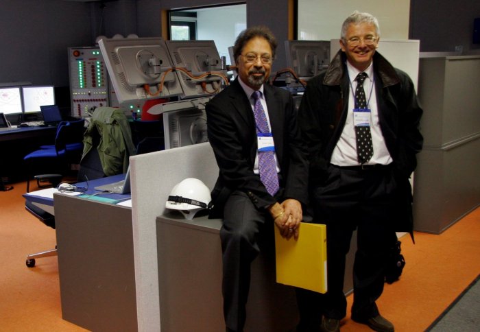 Two men sitting on a desk in a control room