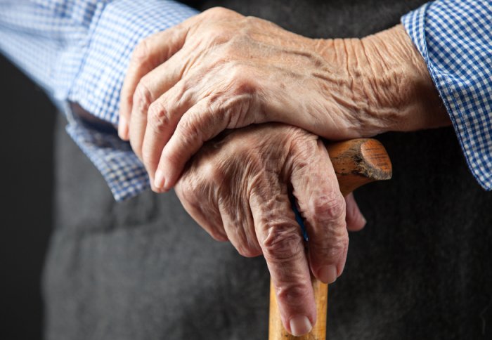 An ageing man's hands hold a walking stick