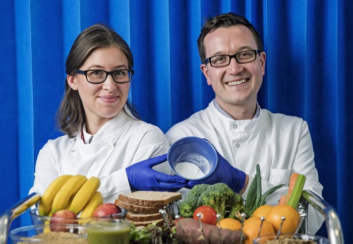 Female and male scientists show their innovative powder, above a selection of fruit, vegetables and grains